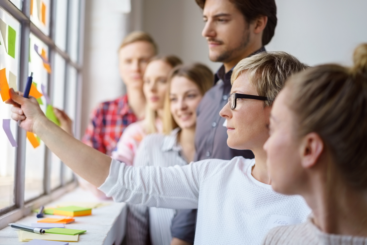 A team of focused work colleagues discussing ideas and brain storming with sticky notes on an office window.