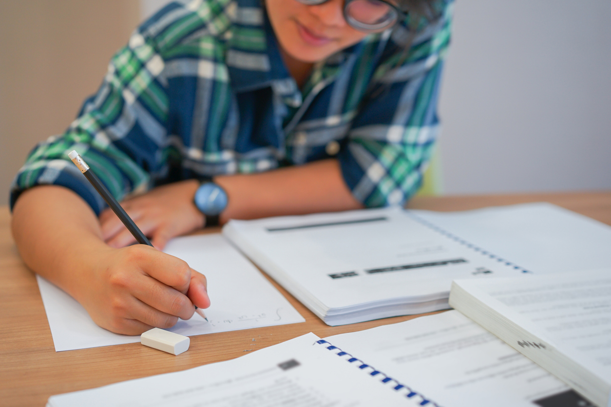 close up young asian student girl using pencil for writing formula of calculus on paper for do homework in library silent zone with textbook , campus lifestyle concept